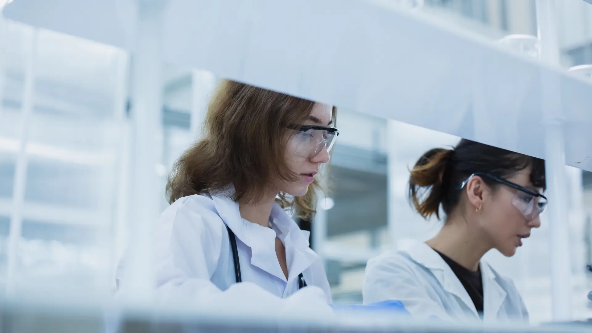 Two laboratory technicians in white coats working behind a cleanroom curtain